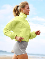 Woman in a bright yellow jacket and gray shorts running on a beach.