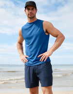 Man wearing a blue sleeveless shirt and navy shorts standing on a beach.