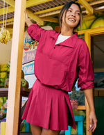 Woman in a red outfit standing in a tropical setting with fruit and colorful decor.