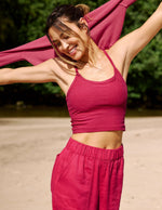 Woman wearing a red cropped tank top and red linen pants stretching on the beach.