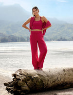 Woman wearing a red cropped tank and linen pants standing on a tree branch in front of the ocean.
