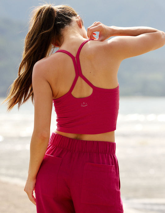 Woman wearing a red cropped tank top and red linen pants with a blurred natural background.