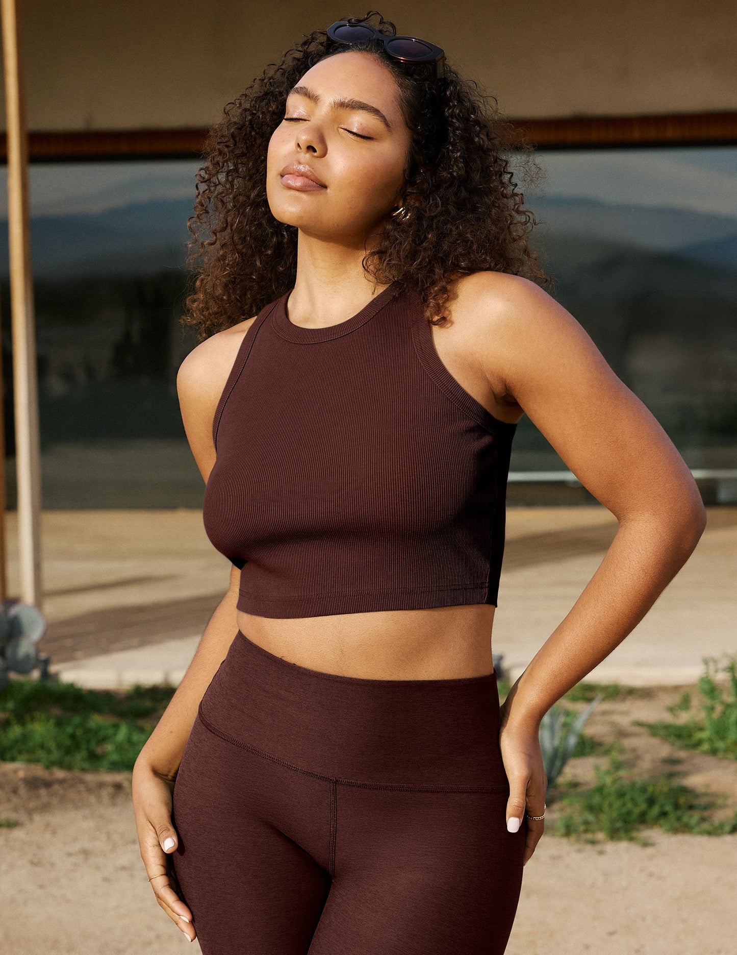 Woman wearing a brown athletic outfit standing outdoors with a blurred background.