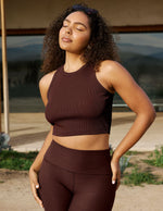 Woman wearing a brown athletic outfit standing outdoors with a blurred background.
