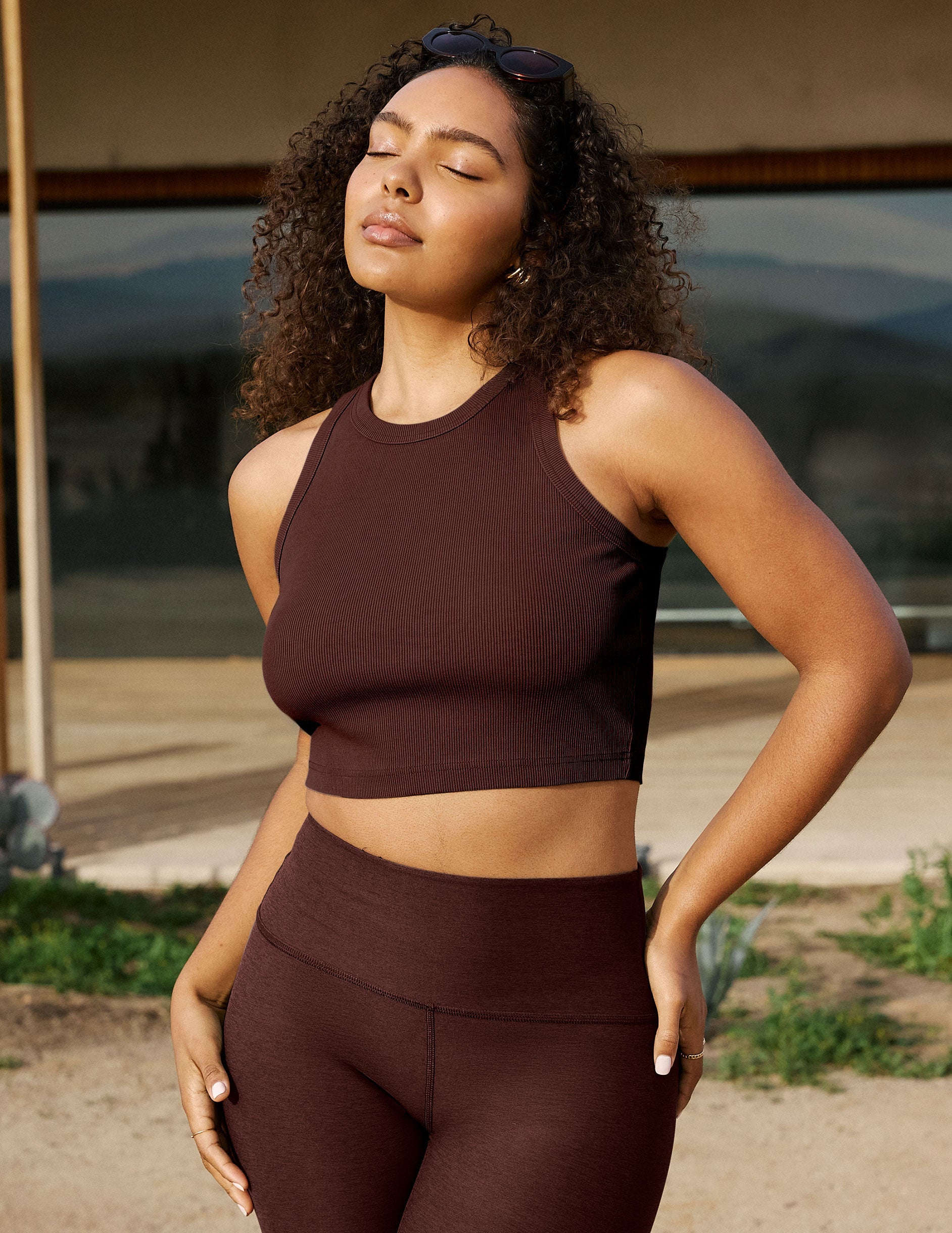 Woman wearing a brown athletic outfit standing outdoors with a blurred background.