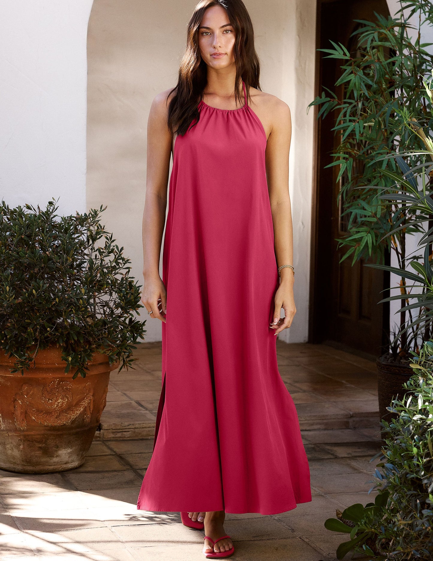 Woman in a red dress standing outdoors with plants around.