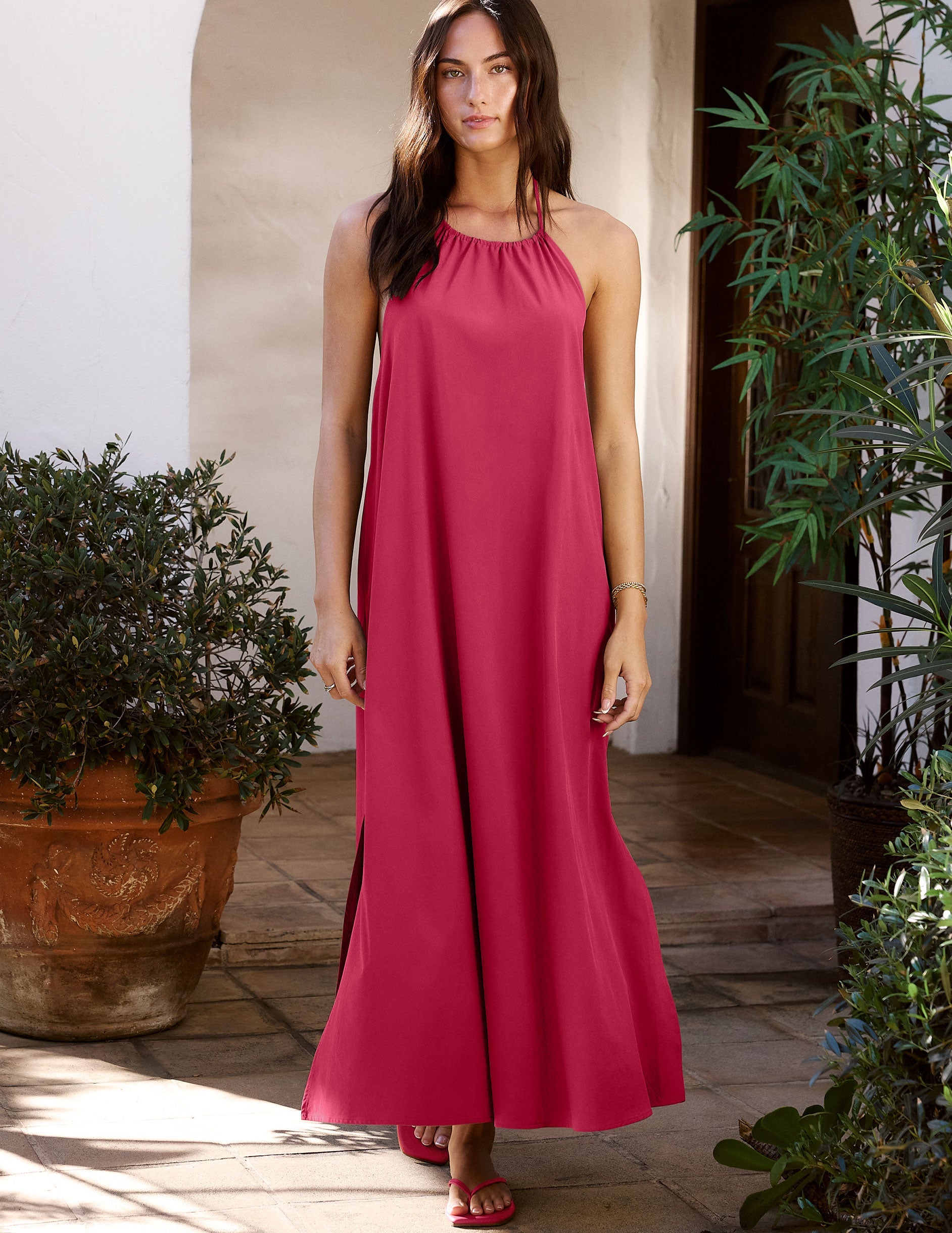 Woman in a red dress standing outdoors with plants around.