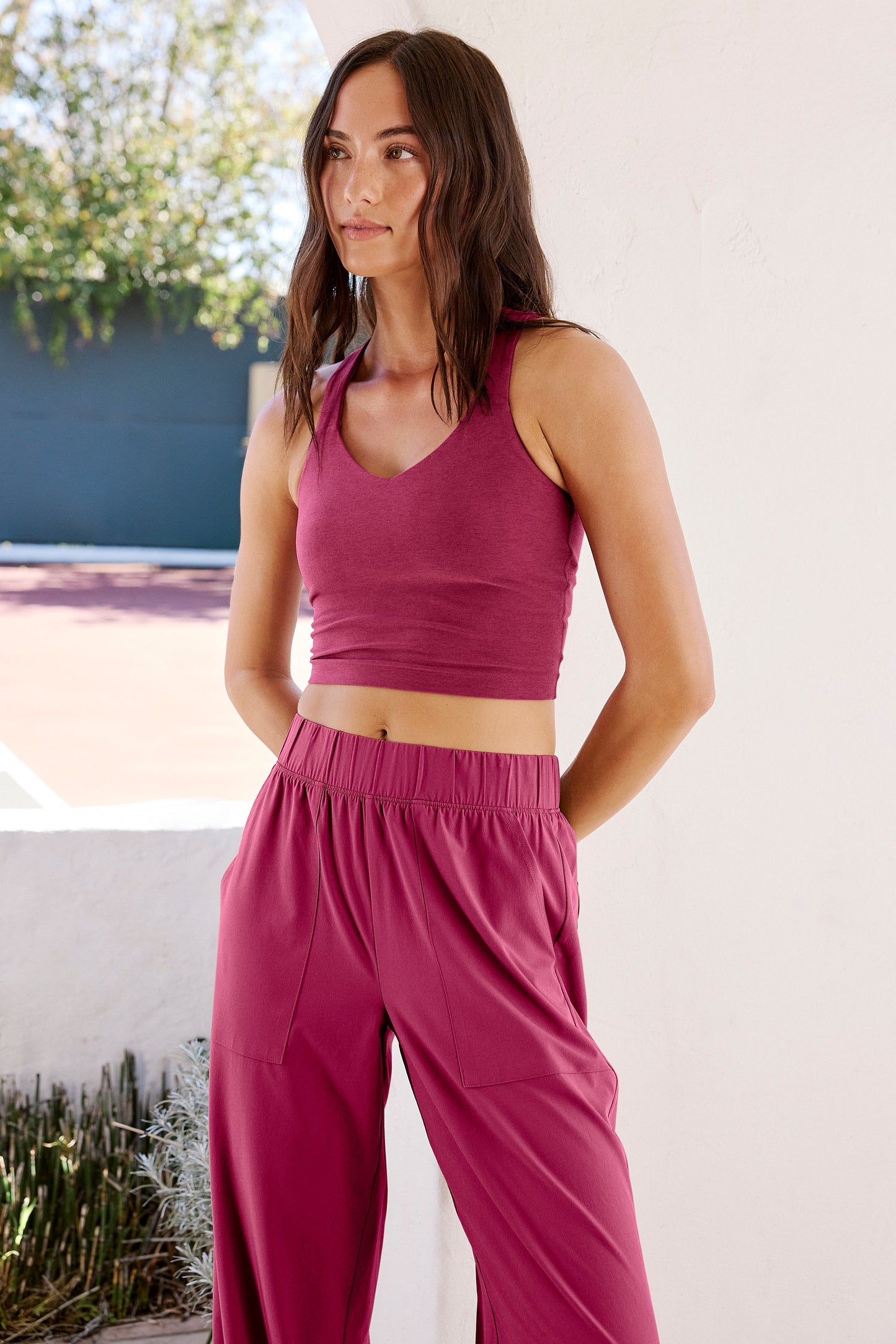 Woman wearing a red cropped tank with a twist cutout back detail and red pants standing in front of a pool.