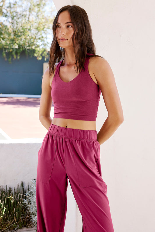 Woman wearing a red cropped tank with a twist cutout back detail and red pants standing in front of a pool.