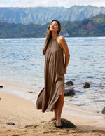 Woman in a brown dress standing on a beach with mountains in the background.