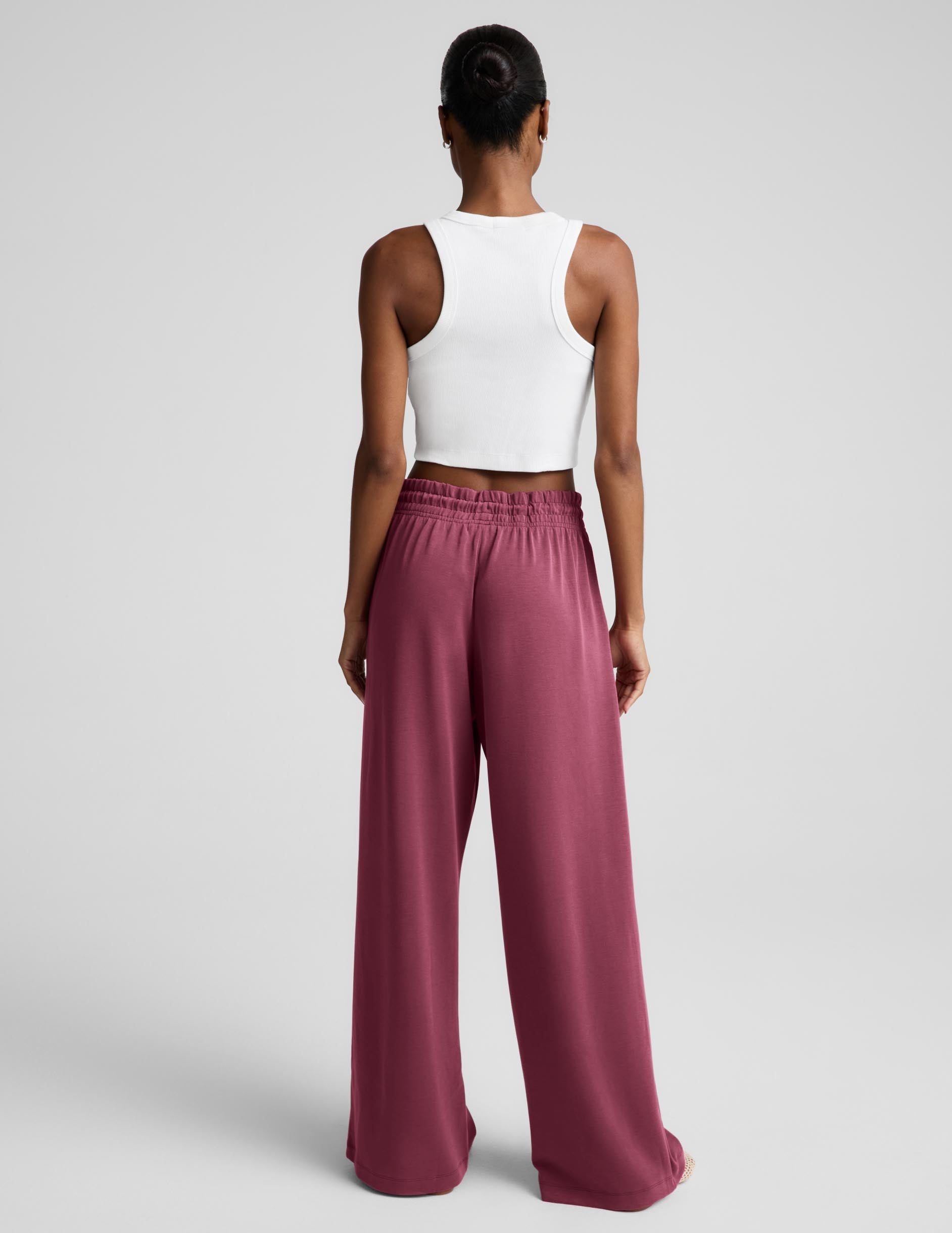 Woman wearing a white ribbed tank top and mauve sweatpants against a plain background.
