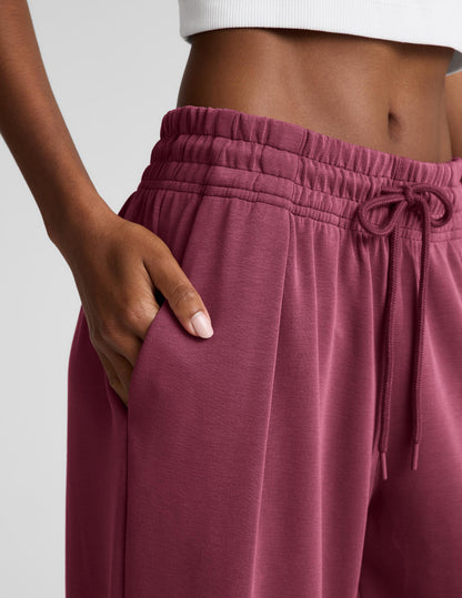 Woman wearing a white ribbed tank top and mauve sweatpants against a plain background.