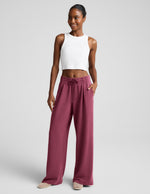 Woman wearing a white ribbed tank top and mauve sweatpants against a plain background.