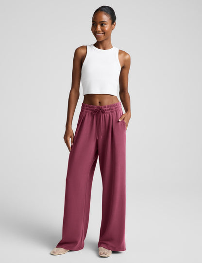 Woman wearing a white ribbed tank top and mauve sweatpants against a plain background.