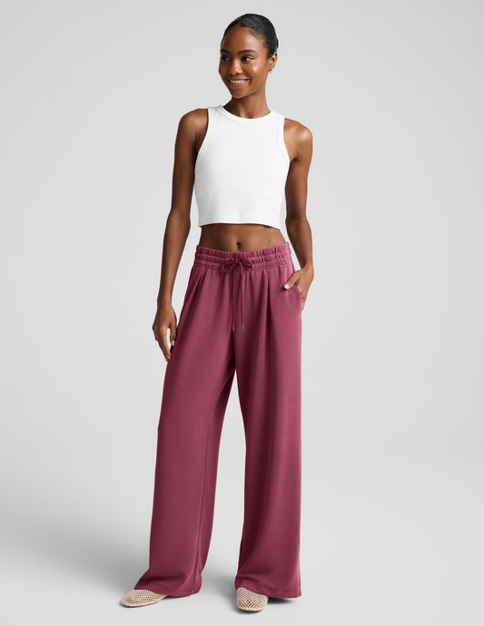 Woman wearing a white ribbed tank top and mauve sweatpants against a plain background.