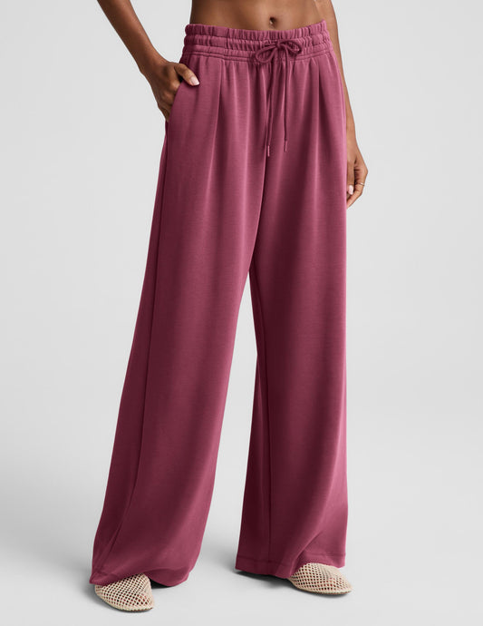 Woman wearing a white ribbed tank top and mauve sweatpants against a plain background.