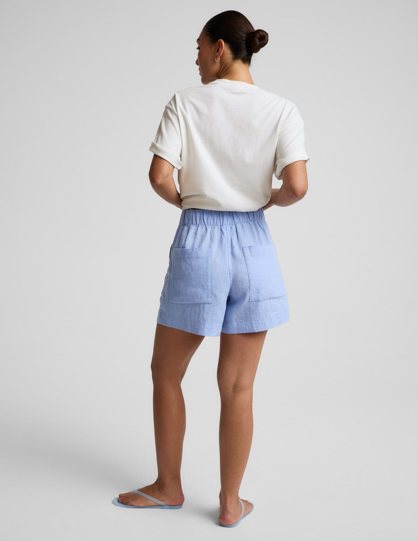 Person wearing light blue shorts and a white top on a plain background.