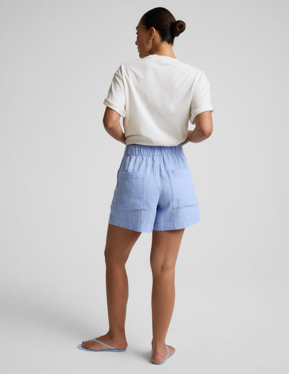 Person wearing light blue shorts and a white top on a plain background.