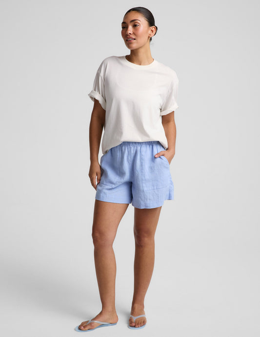 Woman wearing a white cotton t-shirt and blue linen shorts against a plain background.