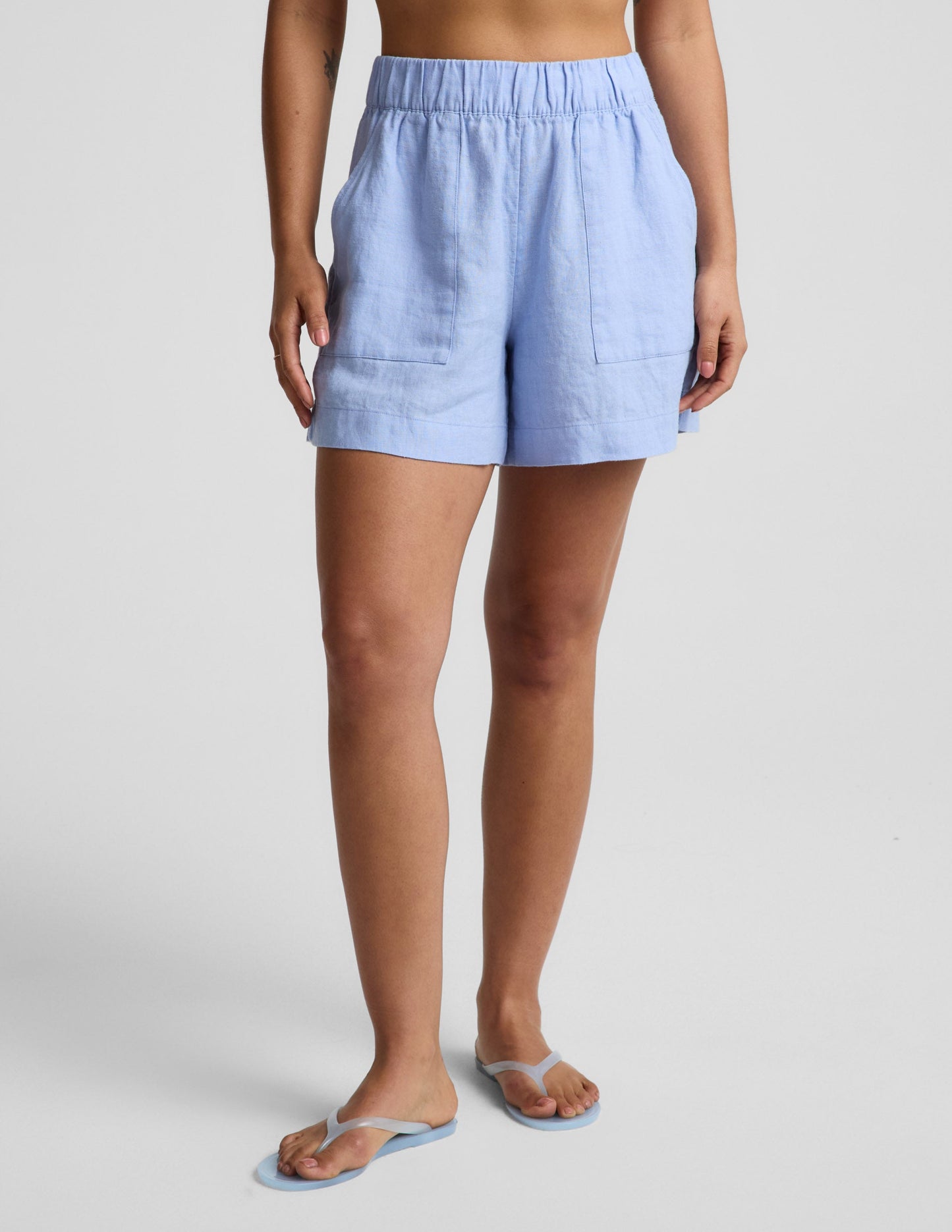 Woman wearing blue linen shorts against a plain background.