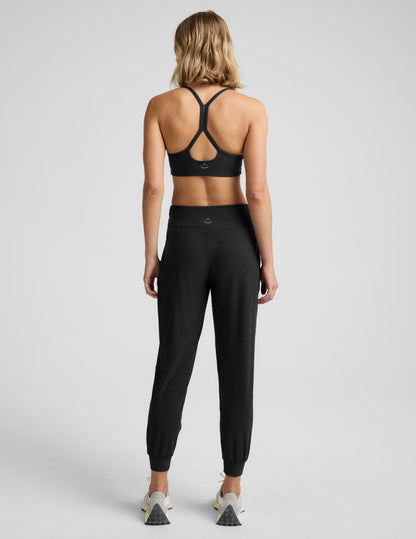 Woman wearing a black bra and black joggers against a plain background.