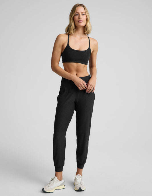 Woman wearing a black bra and black joggers against a plain background.