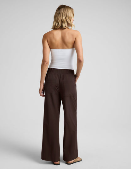 Woman wearing a white halter tank top and brown wide leg pants against a plain studio background.