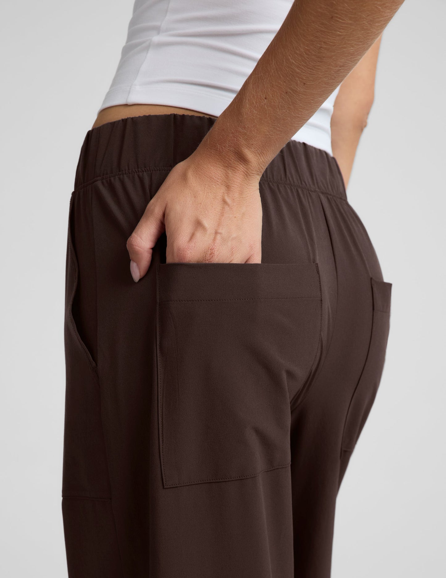Woman wearing a white halter tank top and brown wide leg pants against a plain studio background.
