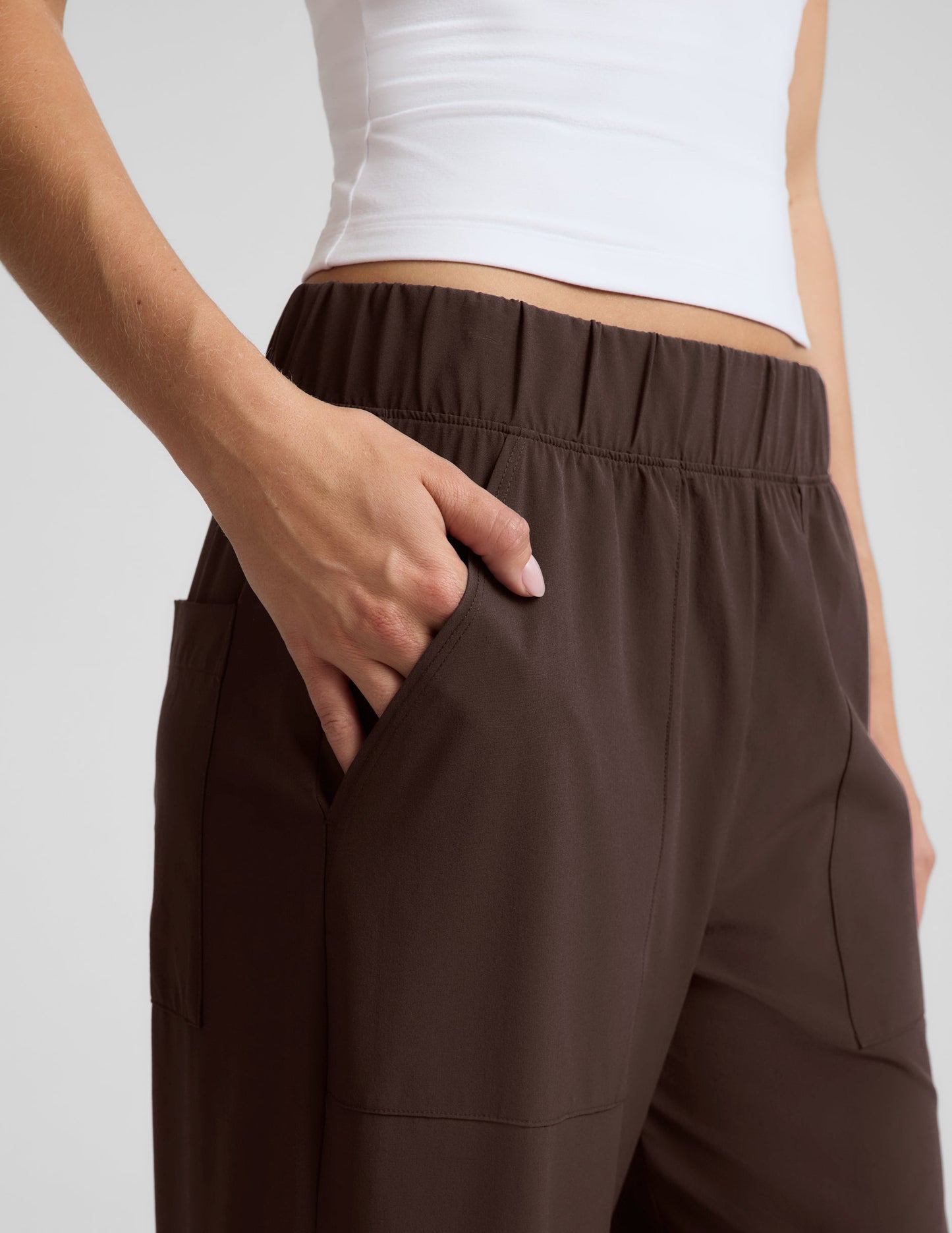 Woman wearing a white halter tank top and brown wide leg pants against a plain studio background.