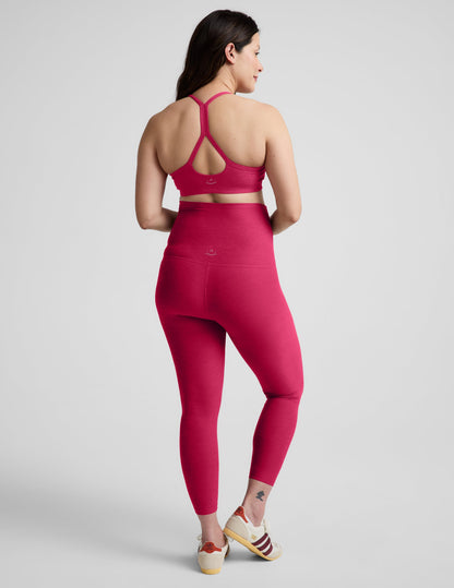 Pregnant woman wearing a red bra and maternity midi leggings against a plain background.