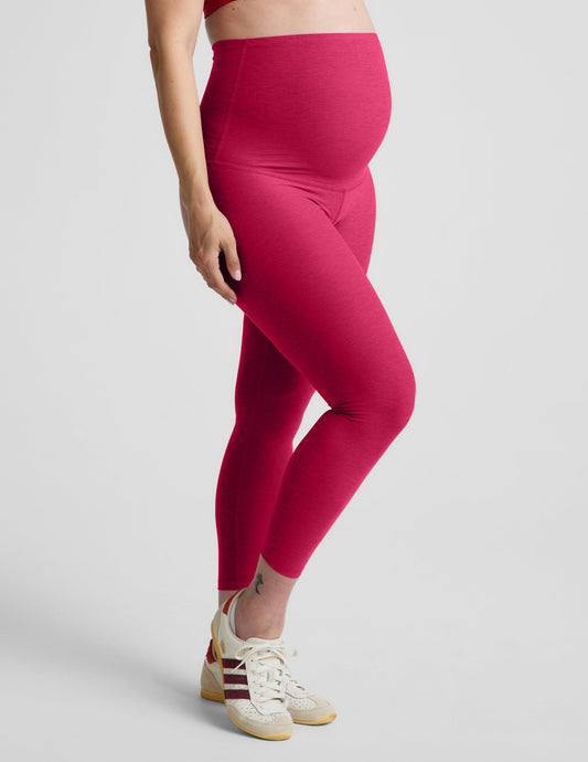 Pregnant woman wearing a red bra and maternity midi leggings against a plain background.