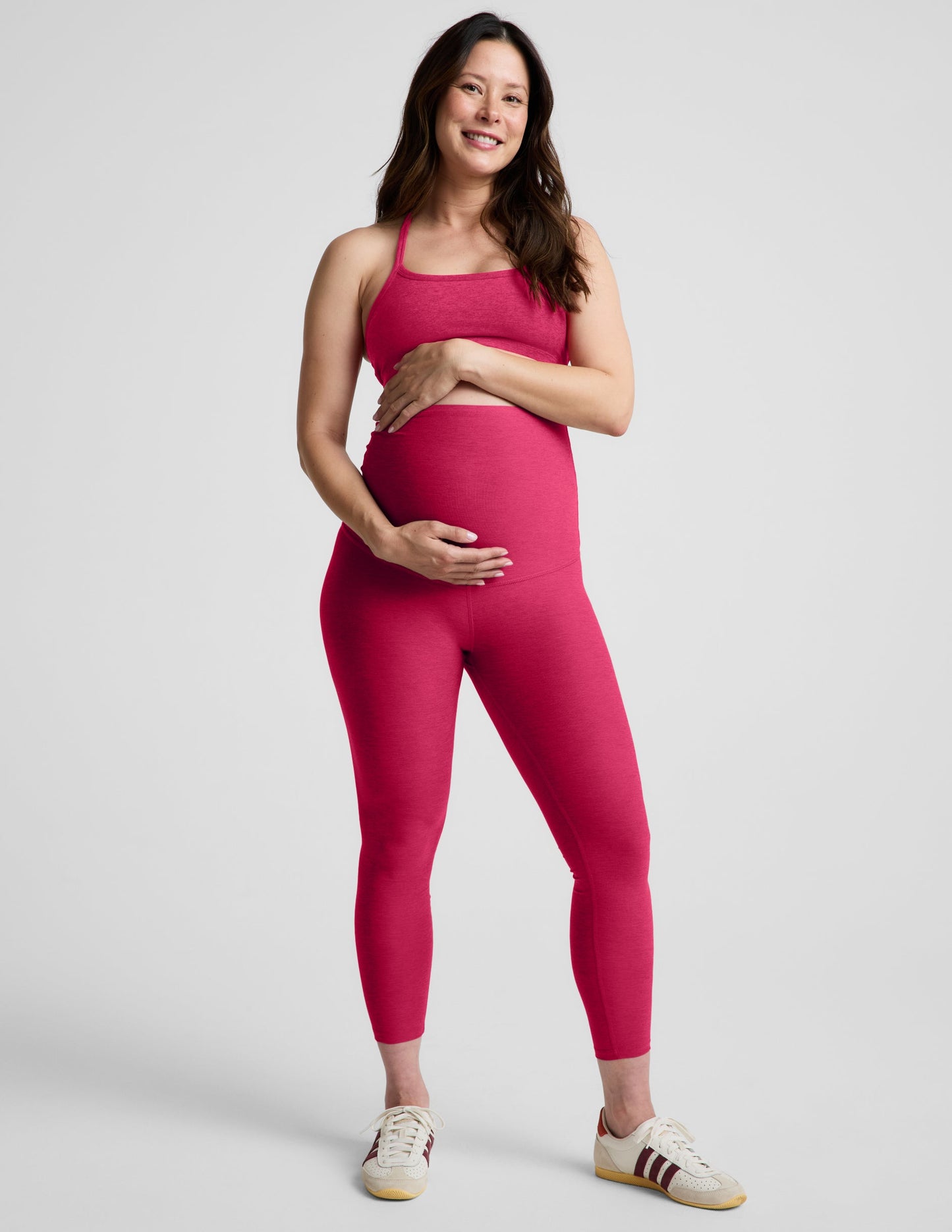 Pregnant woman wearing a red bra and maternity midi leggings against a plain background.