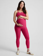 Pregnant woman wearing a red bra and maternity midi leggings against a plain background.
