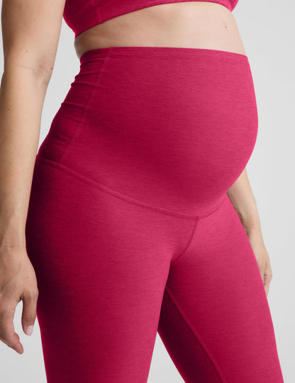 Pregnant woman wearing a red bra and maternity midi leggings against a plain background.