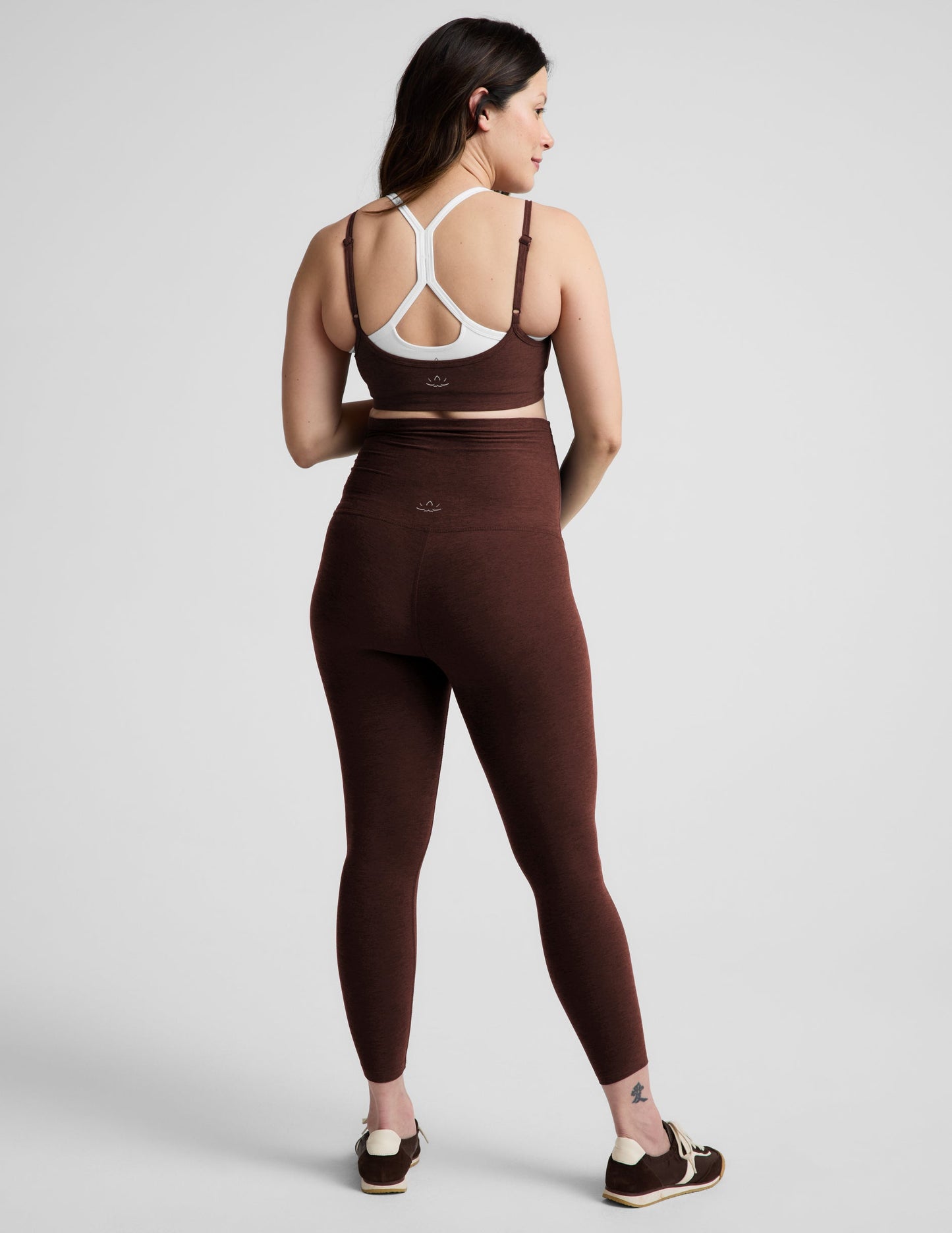Pregnant woman wearing a brown sports bra and brown maternity leggings against a plain background.
