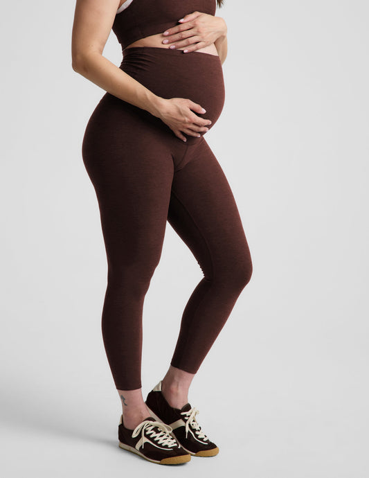 Pregnant woman wearing a brown sports bra and brown maternity leggings against a plain background.