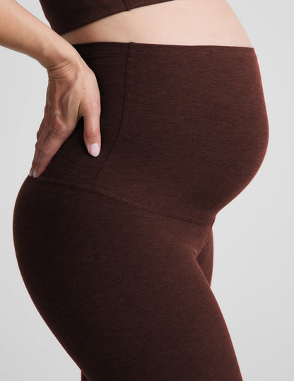 Pregnant woman wearing a brown sports bra and brown maternity leggings against a plain background.