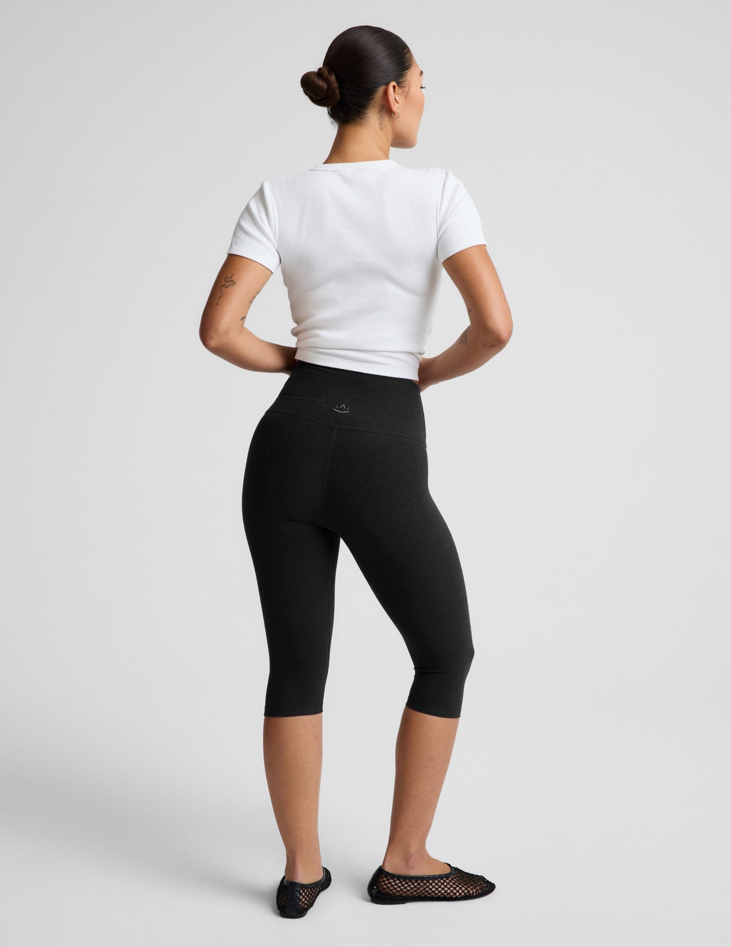 Woman wearing a white ribbed t-shirt and black pedal pusher leggings against a plain background.