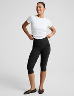 Woman wearing a white ribbed t-shirt and black pedal pusher leggings against a plain background.