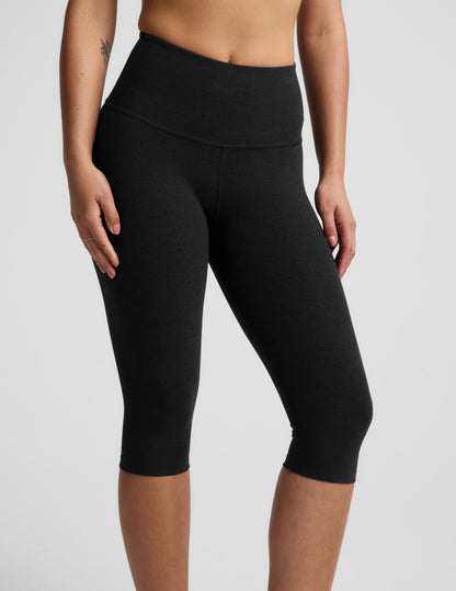 Woman wearing a white ribbed t-shirt and black pedal pusher leggings against a plain background.