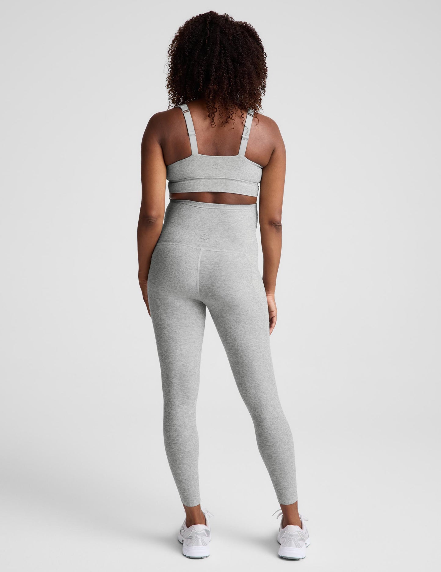 Pregnant woman wearing a gray maternity bra and gray maternity leggings against a plain background.
