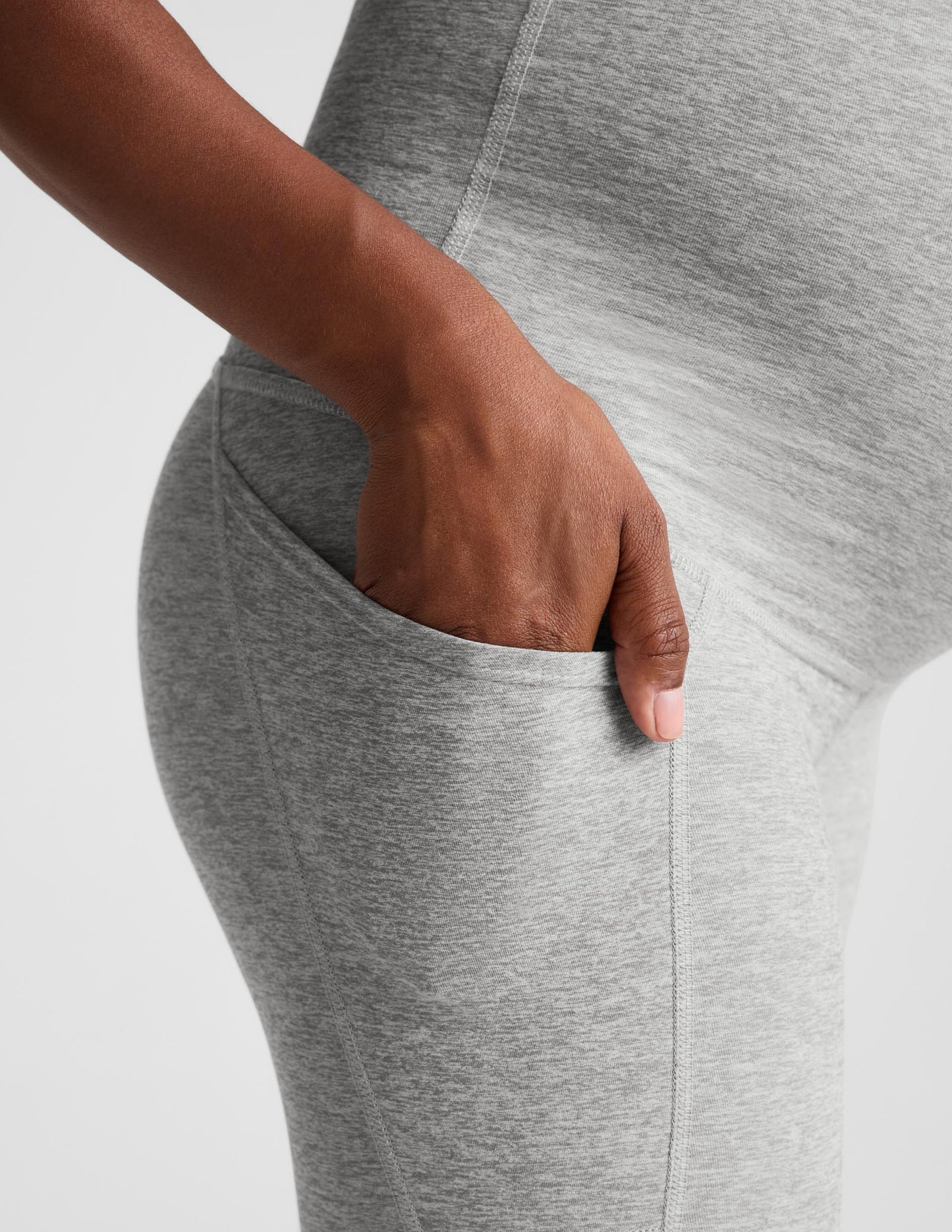 Pregnant woman wearing a gray maternity bra and gray maternity leggings against a plain background.