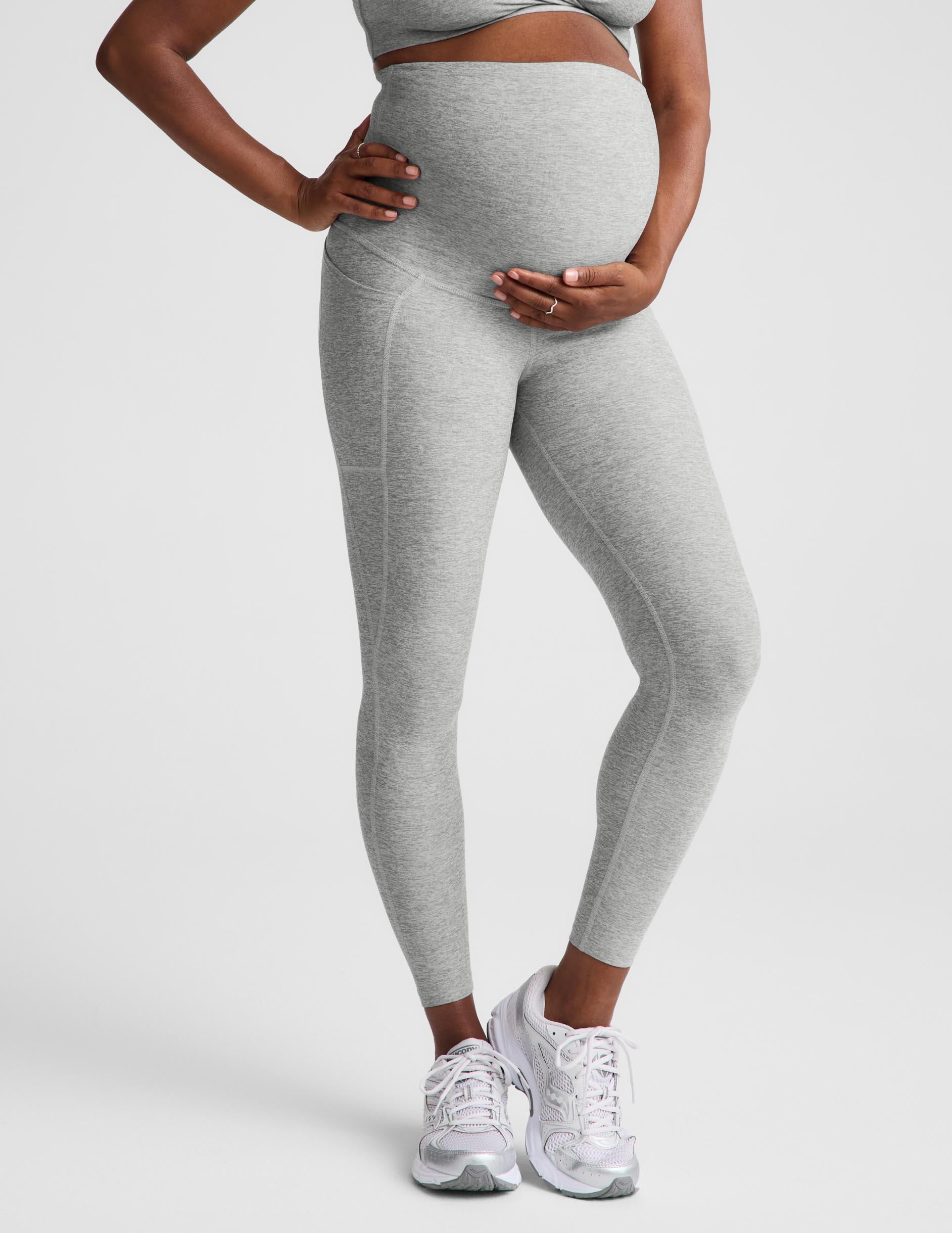 Pregnant woman wearing a gray maternity bra and gray maternity leggings against a plain background.