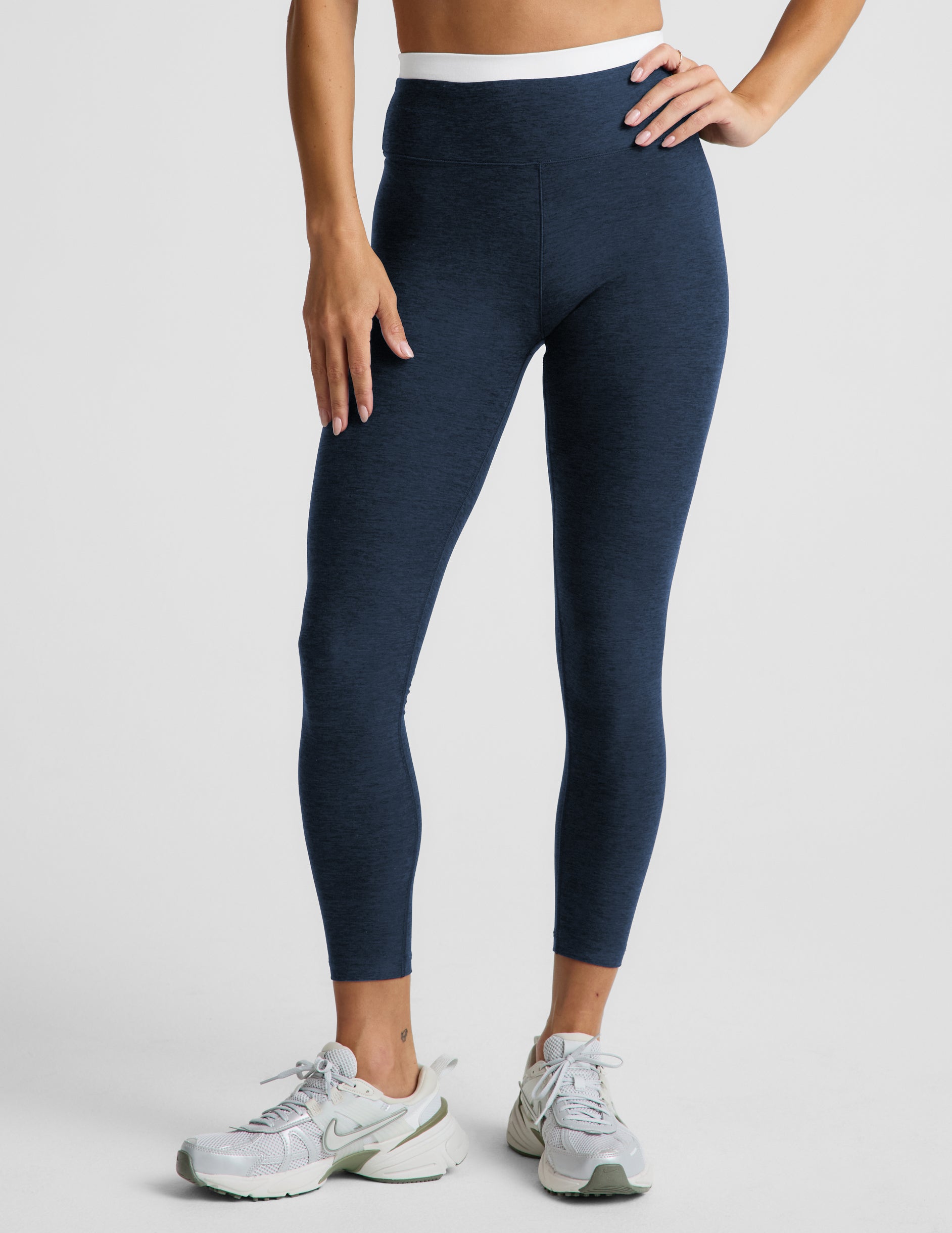 Woman wearing a navy sports bra and leggings set on a plain background.