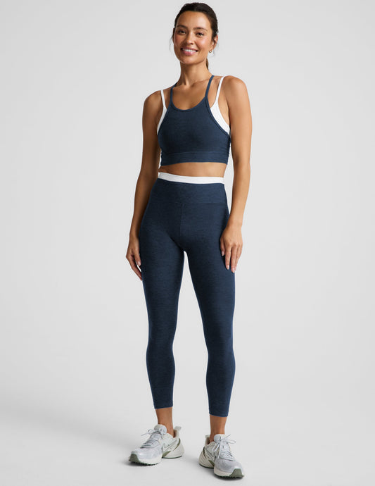 Woman wearing a navy sports bra and leggings set on a plain background.