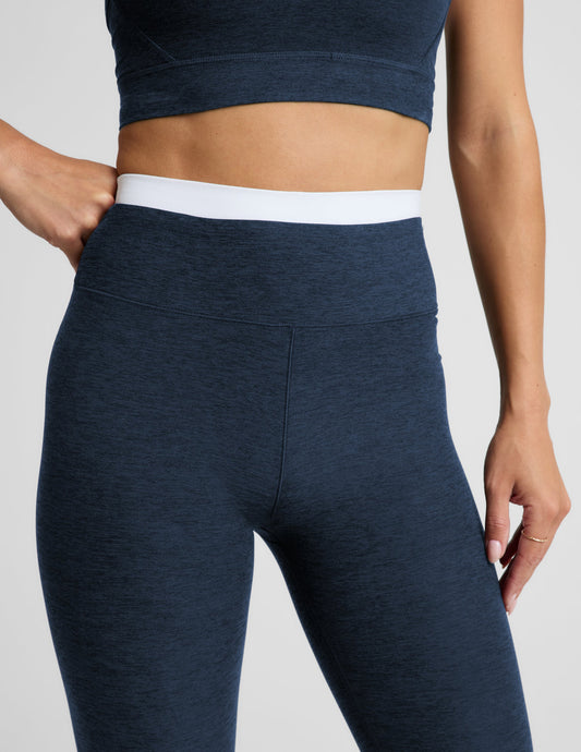 Woman wearing a navy sports bra and leggings set on a plain background.