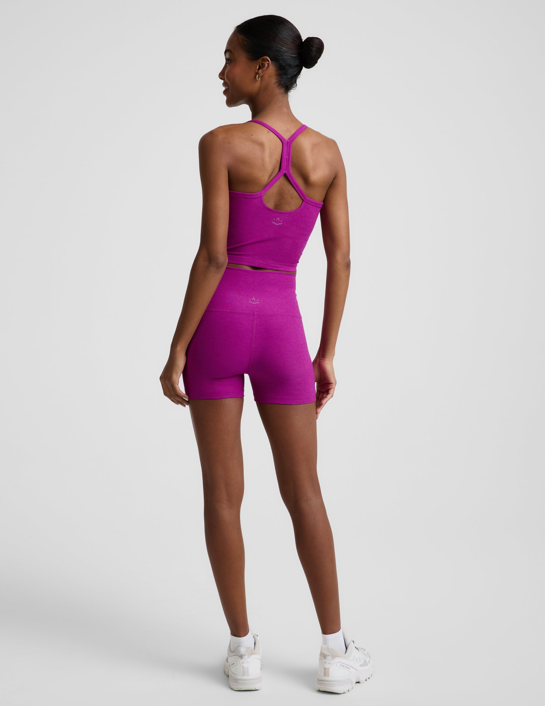 Woman wearing a purple cropped racerback tank and 3" biker shorts against a plain background.