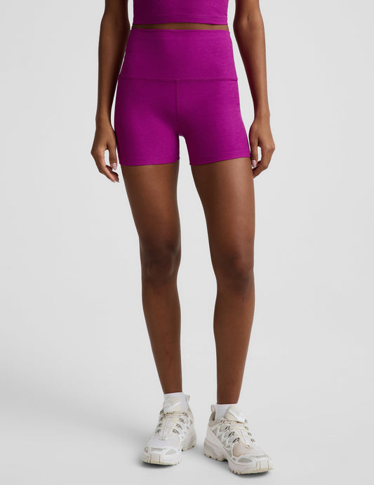 Woman wearing a purple cropped racerback tank and 3" biker shorts against a plain background.