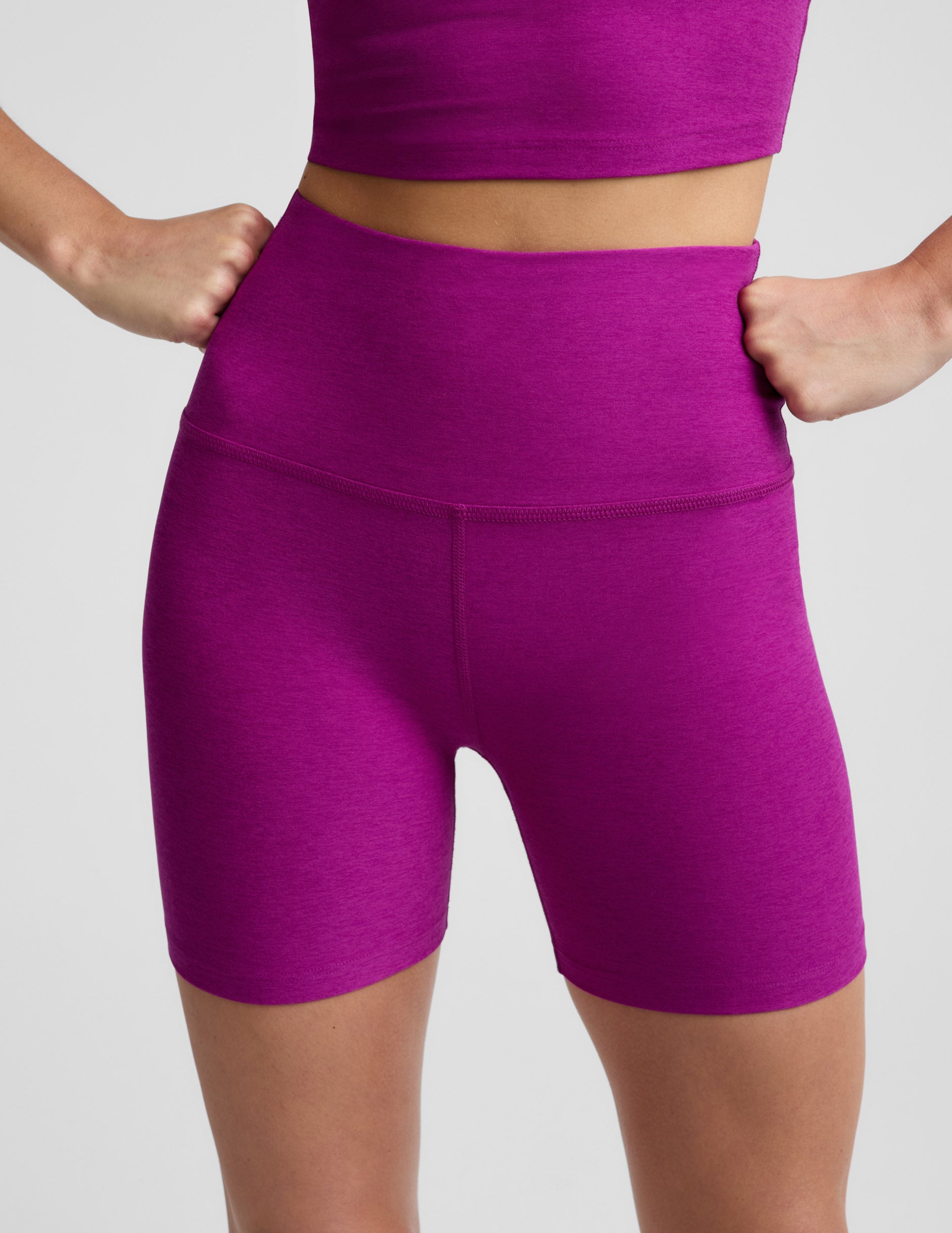 Woman wearing a purple cropped tank top and purple 5" biker shorts against a plain background.