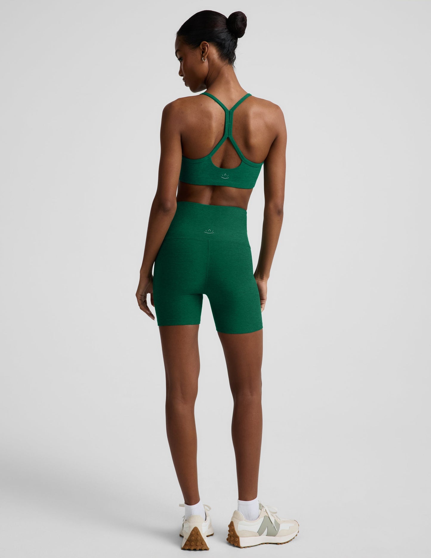 Woman wearing a green racerback bra and 5" biker shorts against a plain background.